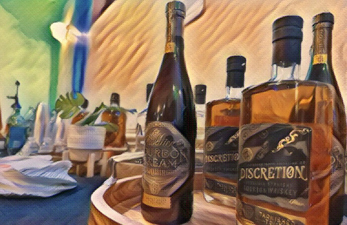 Bottles of sparkling wine and Discretion whiskey lined up on a dressed bar with folded napkins and glassware.