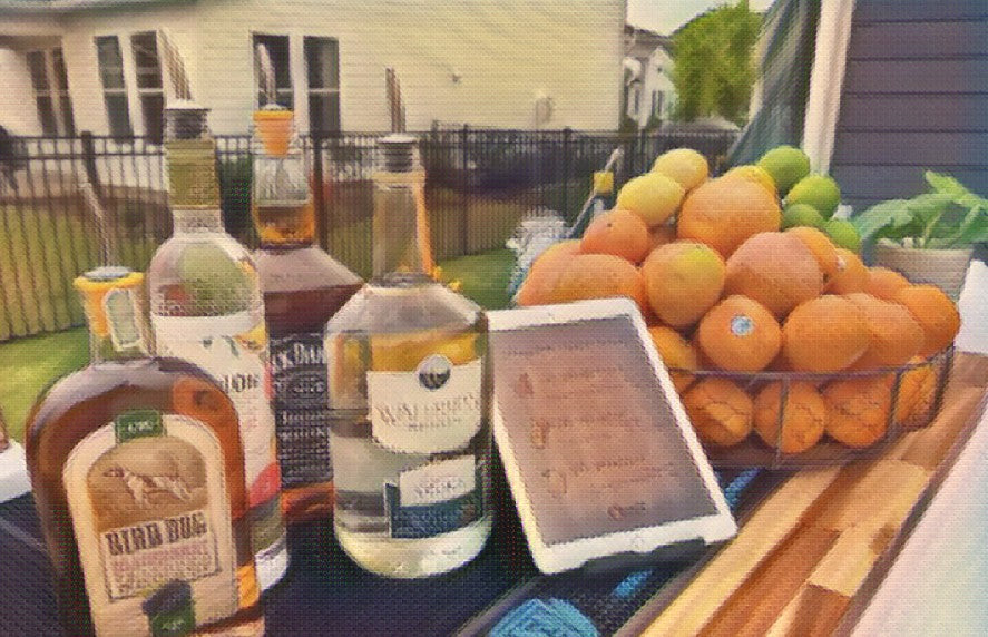 An outdoor bar top with spirits, a printed cocktail menu card and a bowl of fresh oranges.