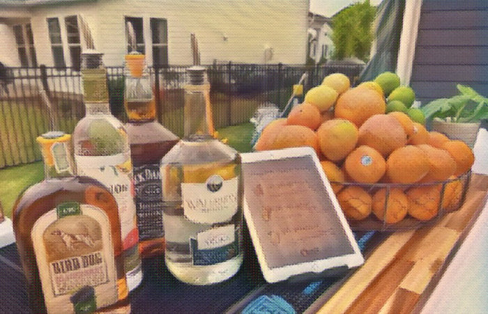 An outdoor bar top with spirits, a printed cocktail menu card and a bowl of fresh oranges.