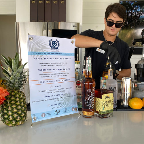 An Executive Beverage bartender at a company party bar with a printed fresh-pressed cocktail menu and a pineapple.