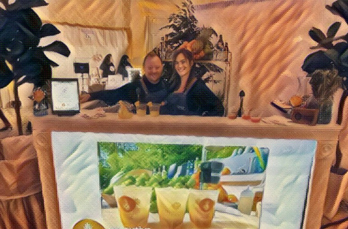 Two Executive Beverage bartenders behind a bar dressed with tropical foliage, glasses of fresh-pressed cocktails on the counter.