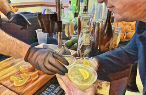 A gloved bartender squeezing fresh citrus into a cocktail beside a board of sliced oranges and lemons.