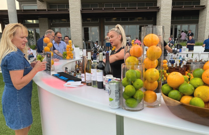 Guests at a white curved Executive Beverage bar stacked with bowls of fresh lemons, limes and oranges.