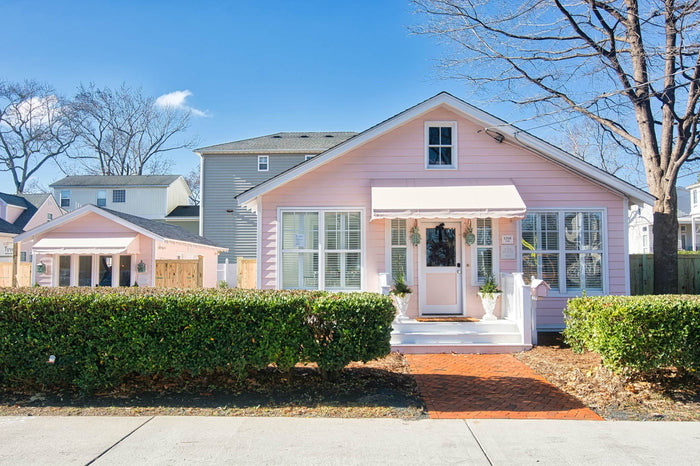 The Pink House, a pale pink event property in Virginia Beach, seen from the street behind clipped hedges.
