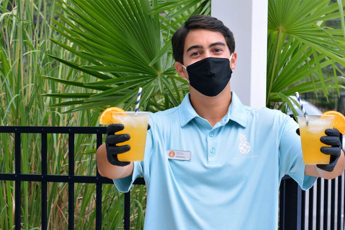 An Executive Beverage bartender in a branded polo holding out two fresh-pressed orange crushes.