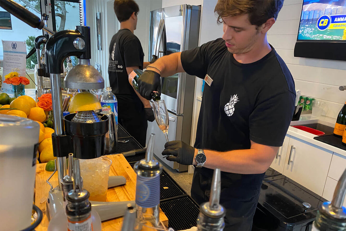 An Executive Beverage bartender working a citrus press at an indoor bar station stacked with oranges.