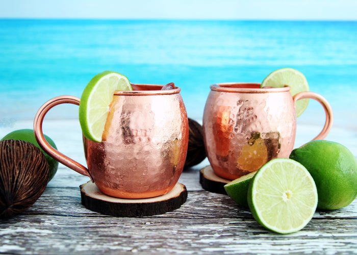 Two copper mugs of Moscow mule garnished with fresh lime against a bright turquoise backdrop.