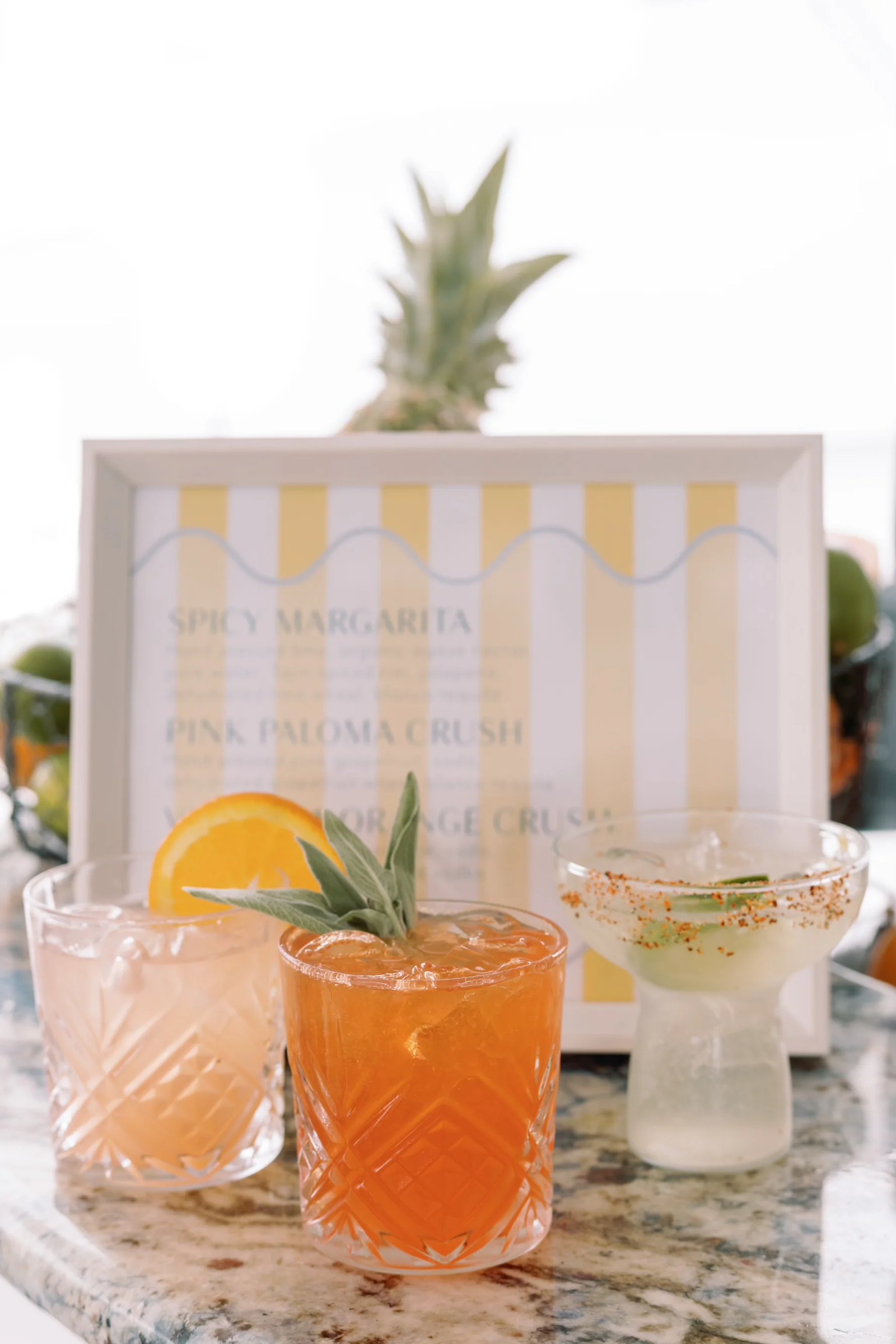 Three signature cocktails lined up in front of a printed wedding bar menu card.