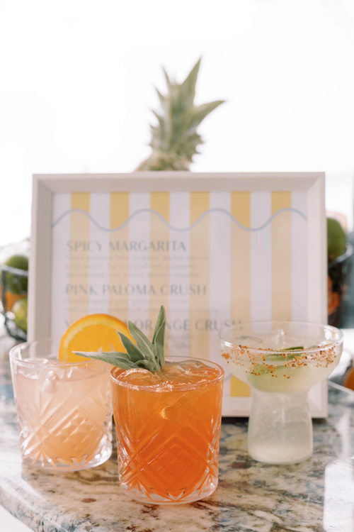 Three signature cocktails lined up in front of a printed wedding bar menu card.