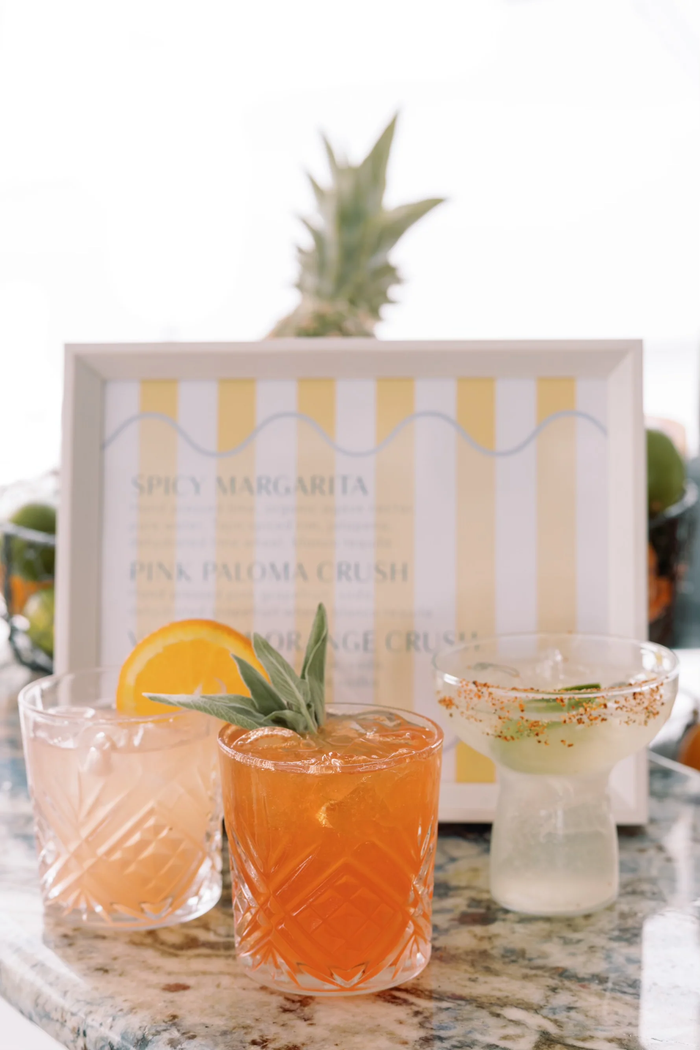 Three signature cocktails lined up in front of a printed wedding bar menu card.
