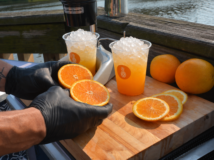 Two fresh pressed orange crushes over pebble ice beside a hand juicer and halved oranges on a butcher's block