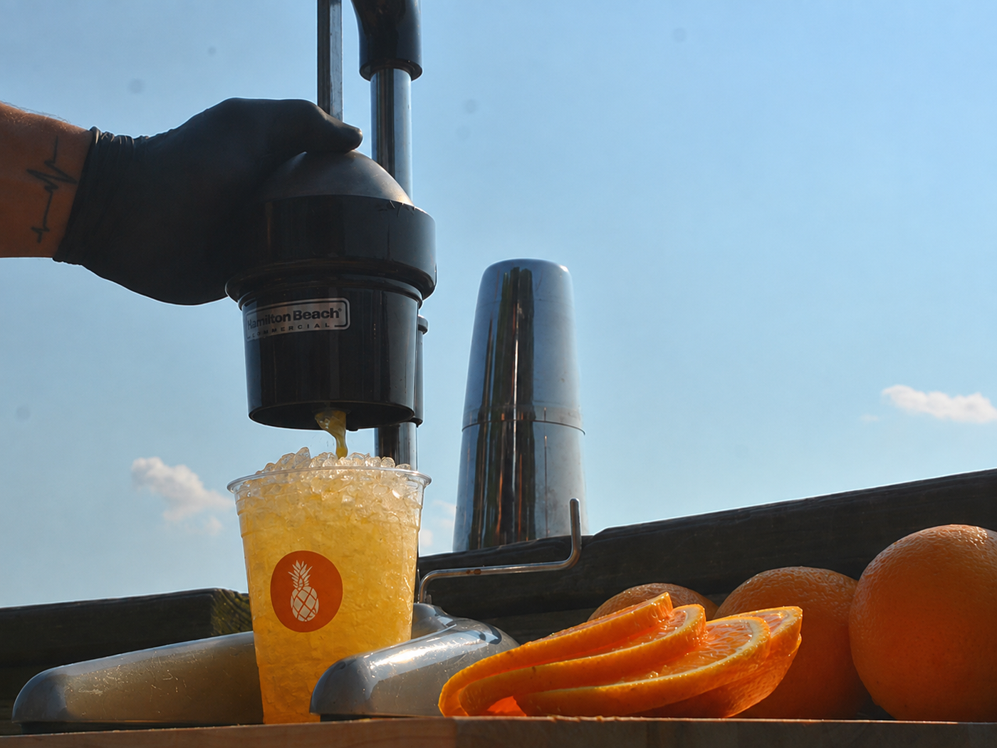 A bartender pressing fresh oranges into a cup for an Executive Beverage Orange Crush made with Waterman's Perfect Crush, halved oranges on the bar alongside.