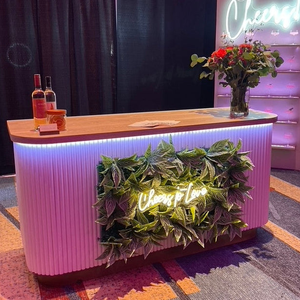 The Magnolia Bar lit in pink with a custom greenery panel and neon signage at an event