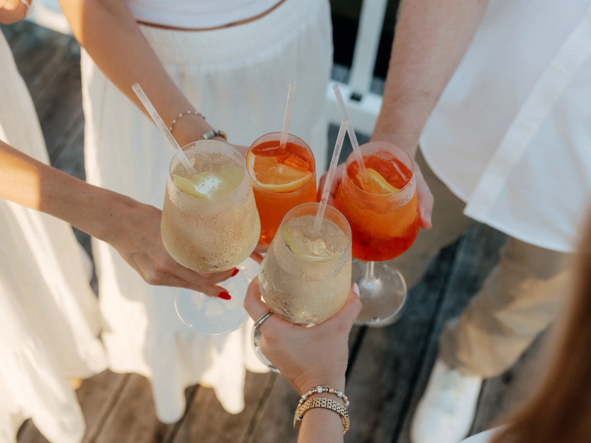 A group toasting with Aperol spritz and Hugo spritz garnished with fresh flowers and orange, served in an Executive Beverage rental wine glass.