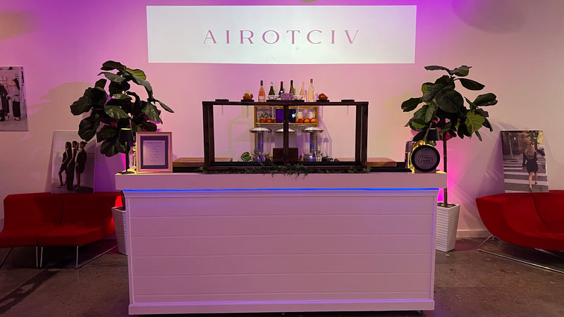 A custom event bar built for Airotciv in Virginia Beach, illuminated white bar front with a lit back-bar of wine and spirits under magenta lighting.