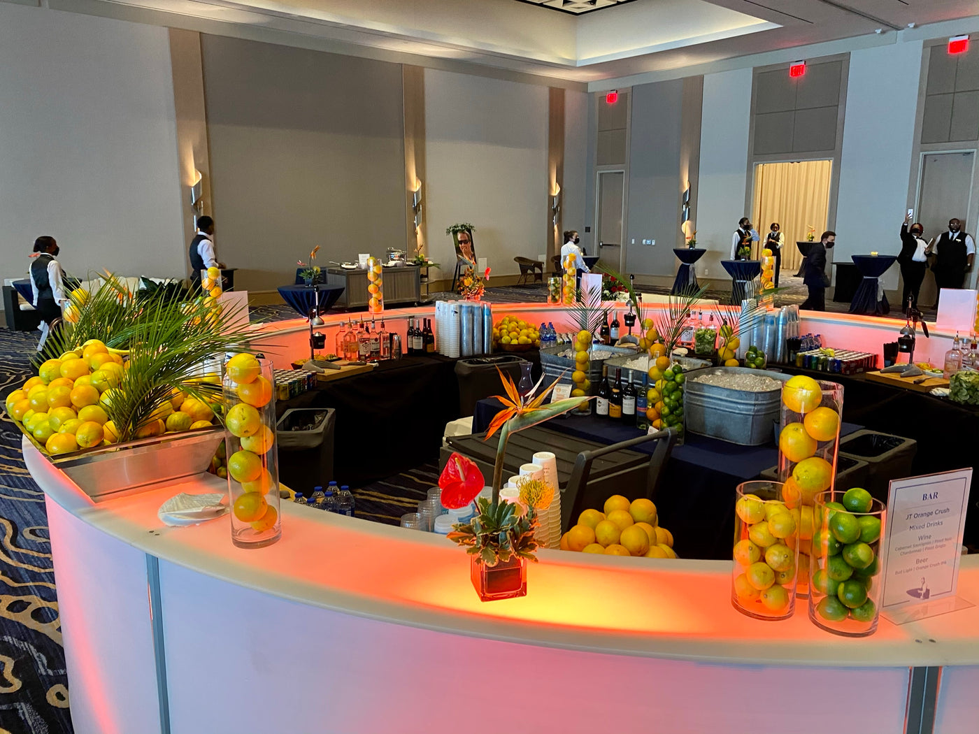A curved LED bar glowing warm in a ballroom, stocked with glass towers of fresh lemons and limes for a corporate event in Hampton Roads.