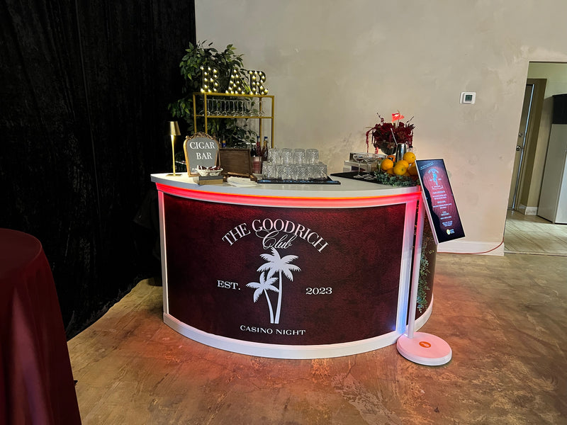 A bar front wrapped in custom vinyl for a private club casino night, with a cigar bar shelf of glassware and florals behind it.