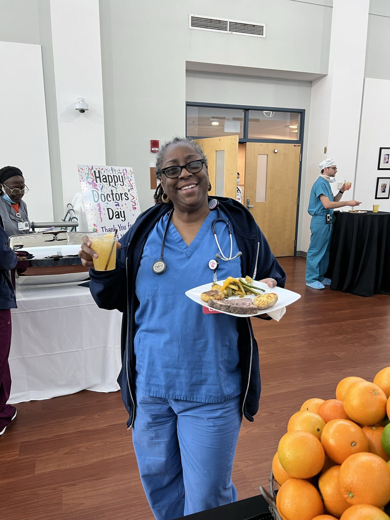 A clinician carrying a plate and a fresh-pressed orange soda past the Happy Doctors’ Day sign at a Sentara staff appreciation lunch in Newport News.