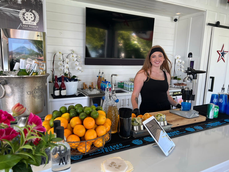 An Executive Beverage bartender working a private home bar in Virginia Beach, a bowl of fresh oranges and limes beside orchids and a chilling champagne bucket.