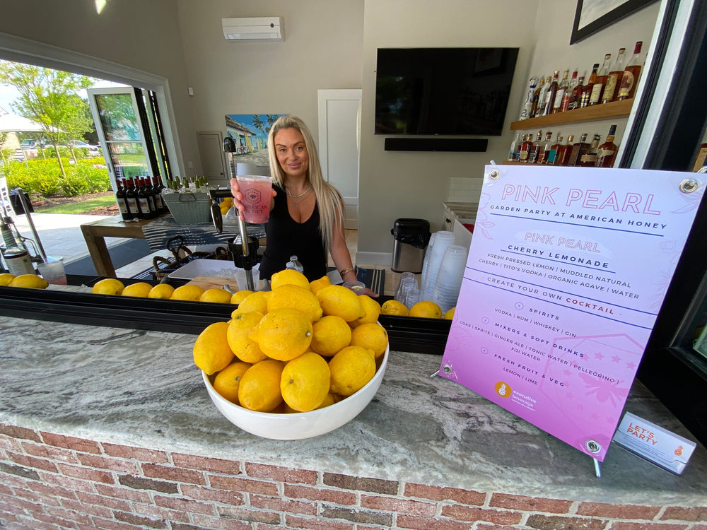 A smiling Executive Beverage bartender serving a cherry lemonade cocktail at a garden party in Virginia Beach.