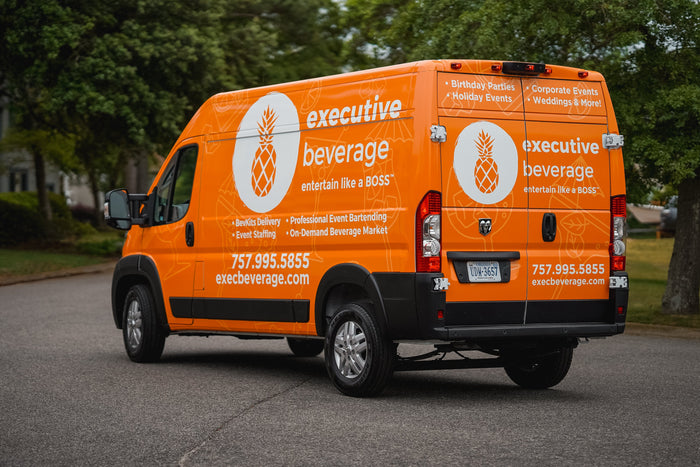 The orange Executive Beverage delivery van, branded with the pineapple logo, parked on a residential street in Hampton Roads.