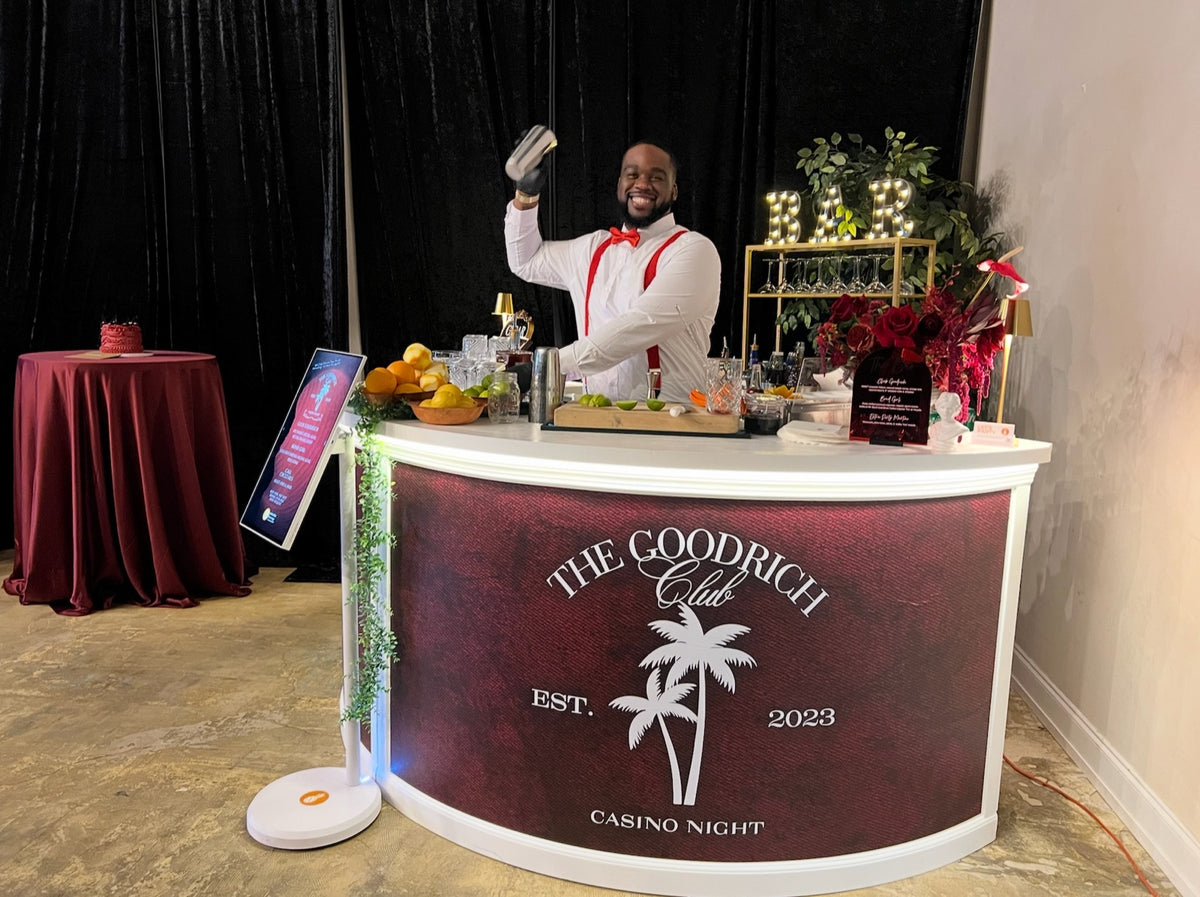 An Executive Beverage bartender shaking a cocktail behind a custom-branded bar with a lit BAR sign at a Norfolk event.
