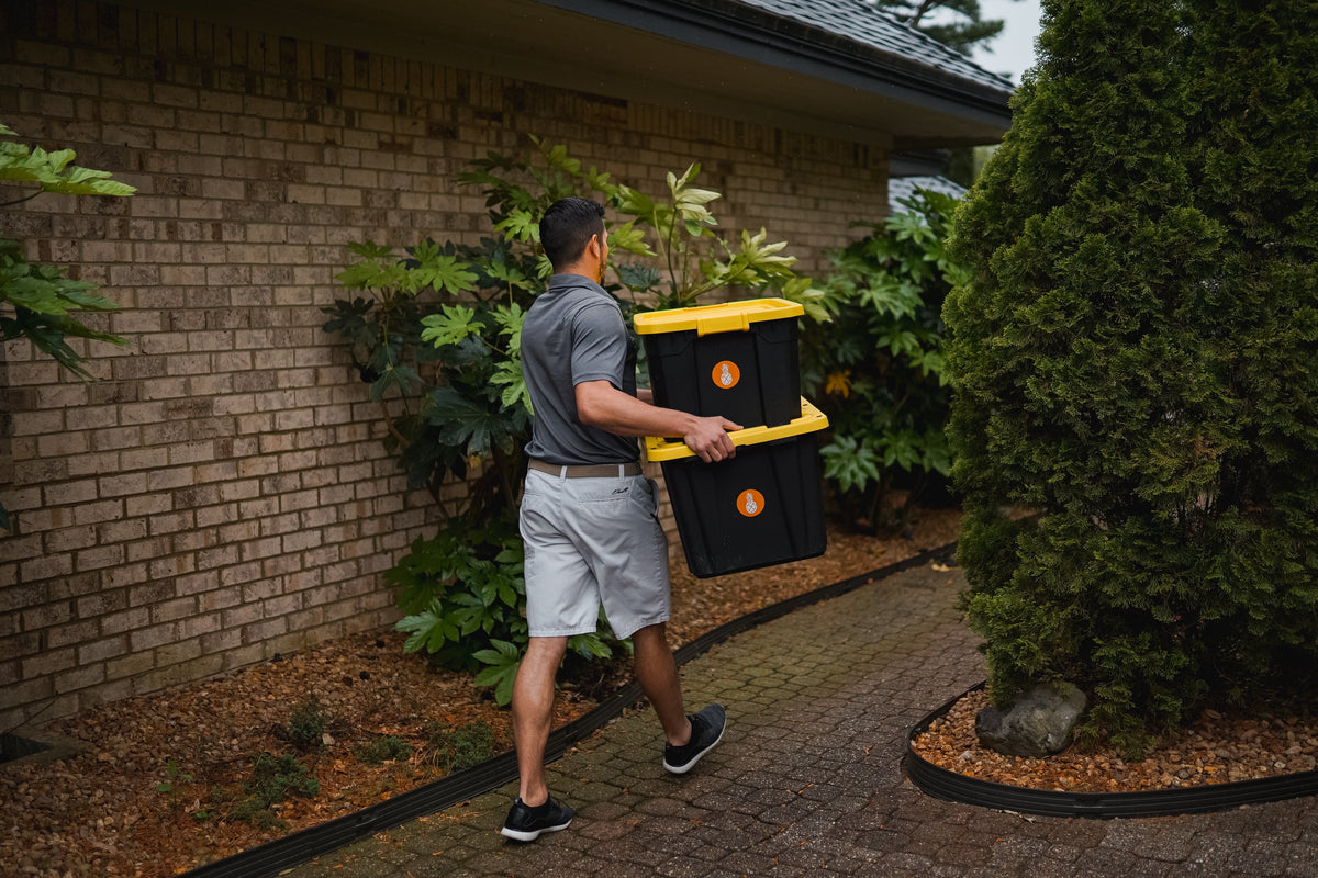 An Executive Beverage driver carrying two stacked equipment crates up a garden path to a front door in Virginia Beach.