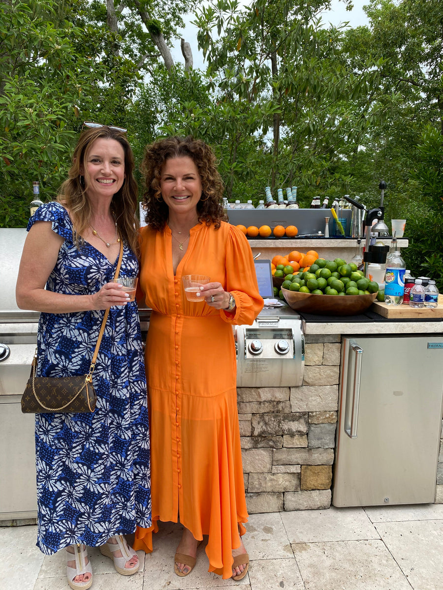 Two guests with cocktails beside an outdoor kitchen island dressed as a bar with fresh citrus, spirits and glassware by Executive Beverage.