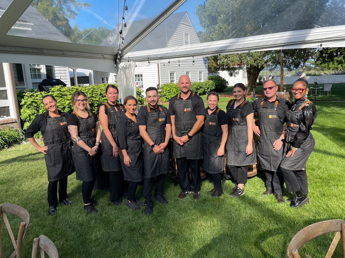 The Executive Beverage bartending crew in branded aprons under a clear tent at an outdoor wedding in Virginia Beach.