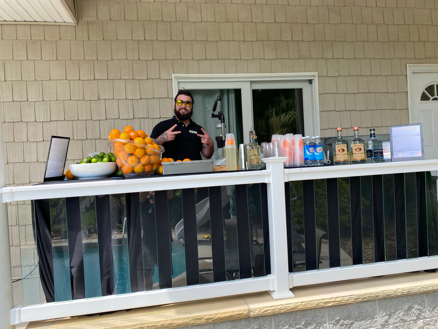 An Executive Beverage bartender working a poolside deck bar at a beach house, fresh citrus and spirits set along the rail.