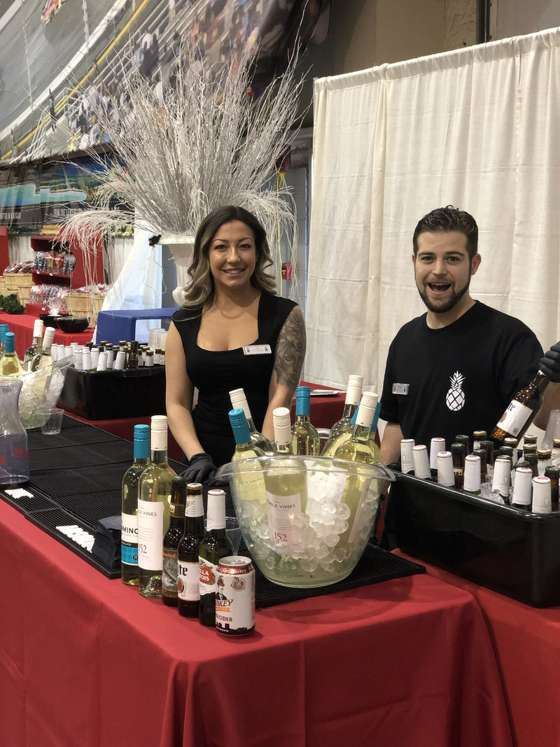 Executive Beverage bartenders pouring wine at the Bizarre Bazaar in Richmond, bottles chilling beside a red-draped bar.