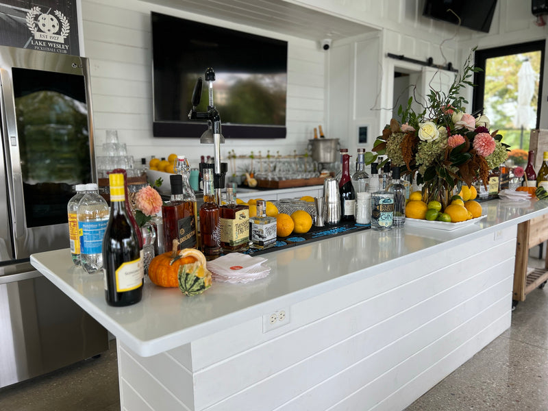 A styled event bar at a private waterfront home, dressed with autumn florals, pumpkins, wine and bowls of fresh citrus before guests arrive.