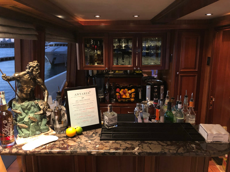 The wood-panelled yacht bar aboard Antares during Art Basel Miami Beach, spirits and fresh oranges set beside the custom cocktail menu.